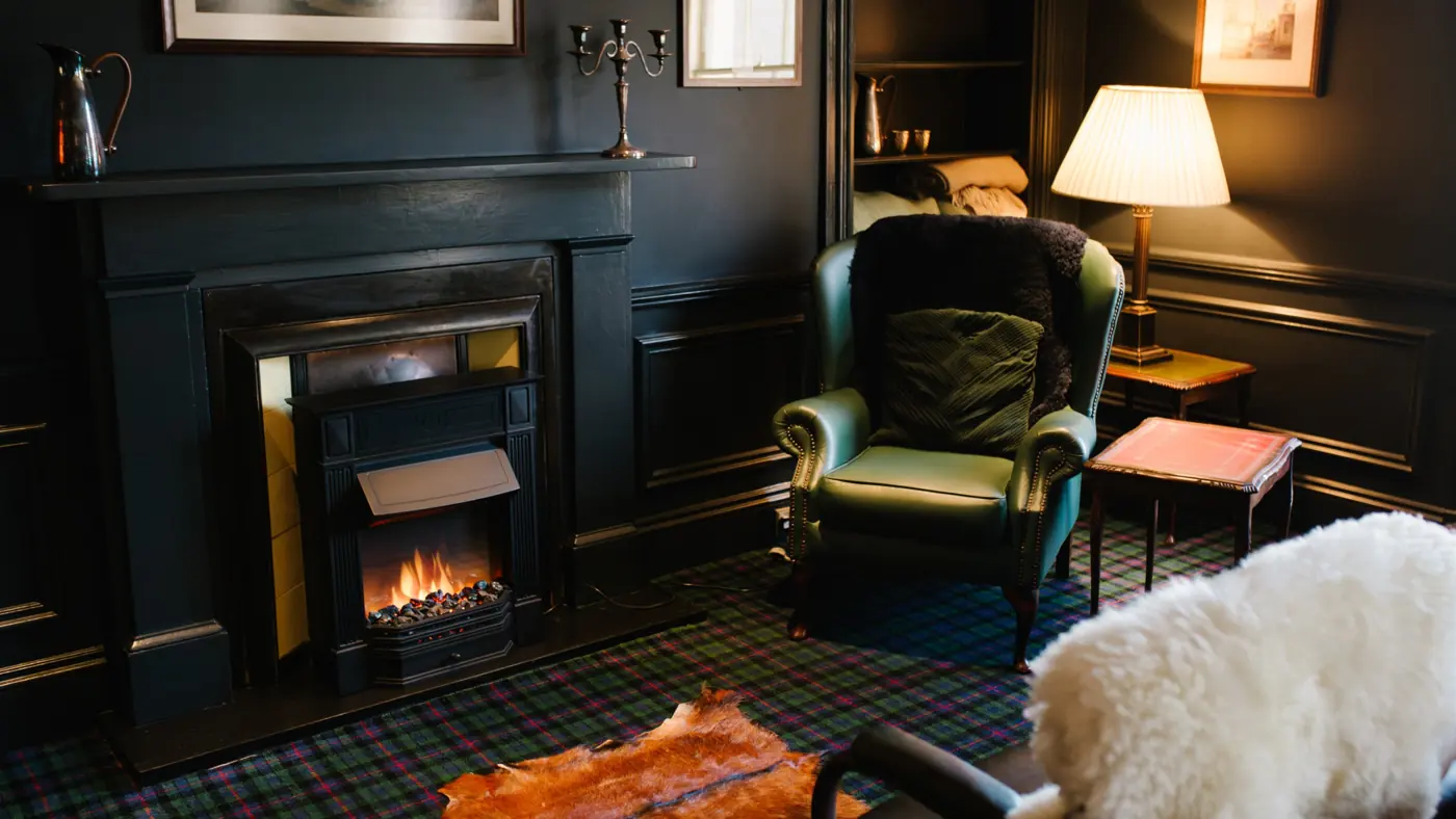 A green leather wing chair beside the fireplace in the Heavey Room