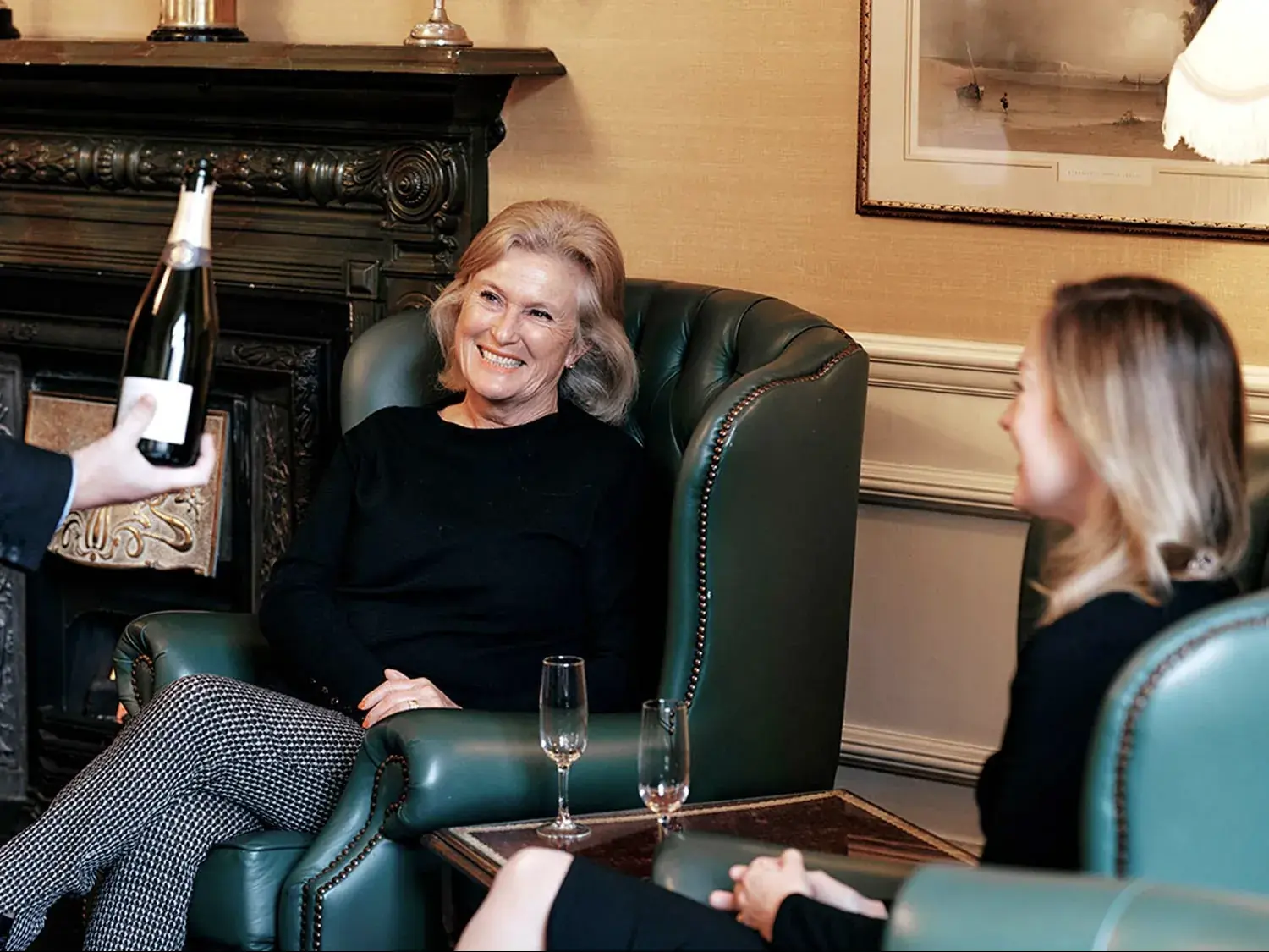 Members sharing a bottle of champagne beside the fireplace