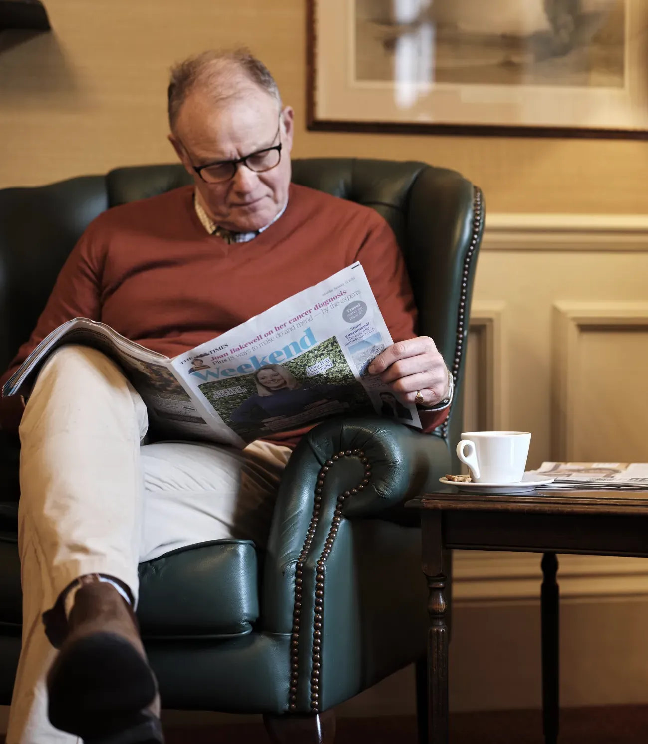 A member reading the paper with a coffee in a green leather wing chair